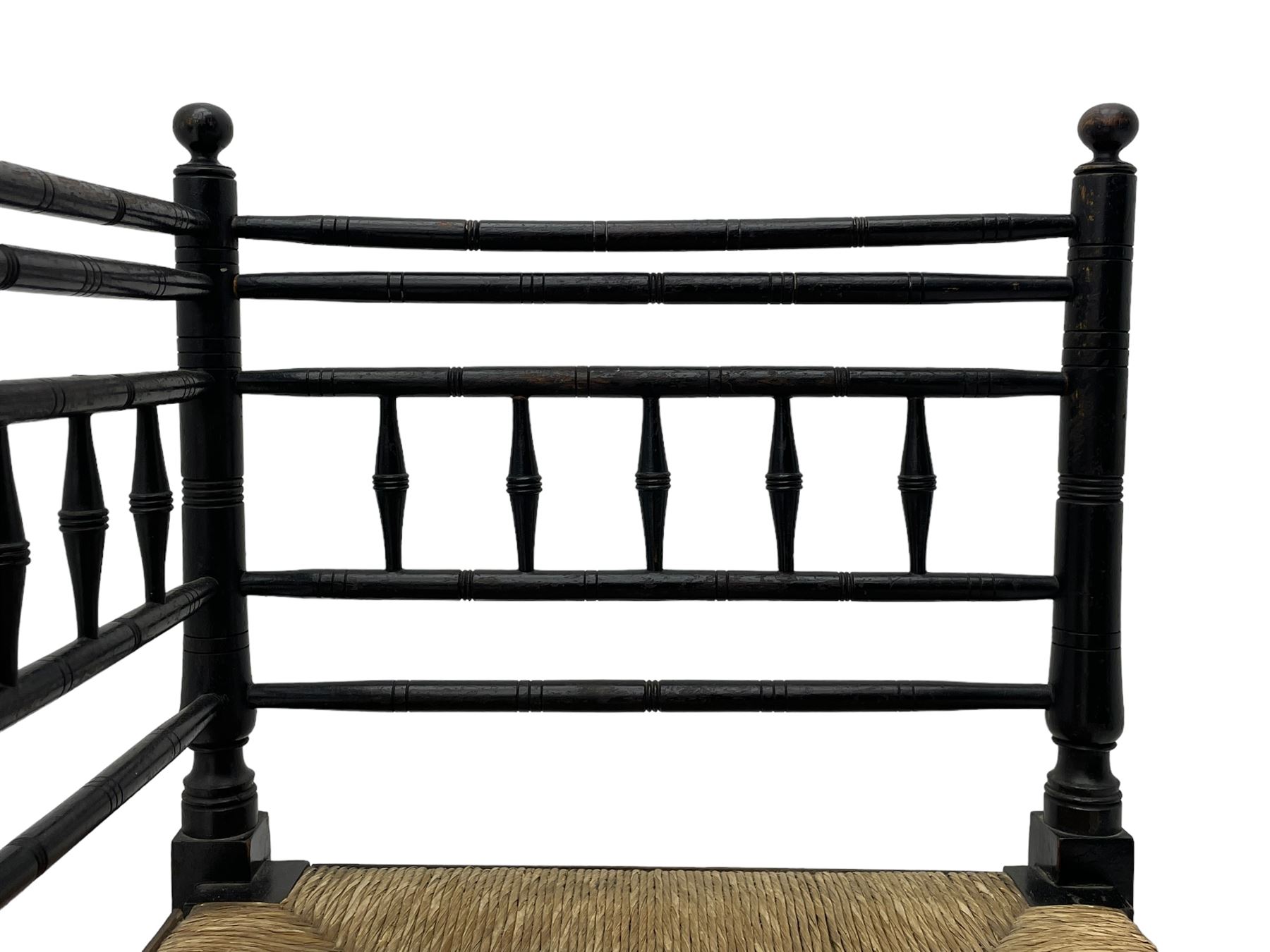 In the manner of William Morris - Arts & Crafts period corner chair, swell turned horizontal rails with balustrade back, rush seat on ring turned supports, black paint finish 