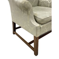 Georgian mahogany framed wingback armchair, upholstered in floral pattern silk damask fabric, wide seat enclosed by rolled arms, on chamfered square supports united by plain stretchers 