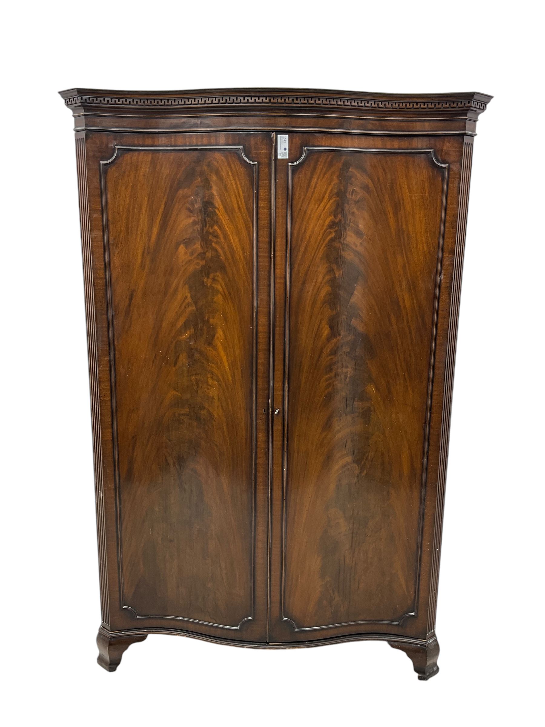 Early 20th century mahogany serpentine double wardrobe, moulded cornice over two figured doors, the interior fitted with hanging rail and shelf, canted and fluted uprights, on bracket feet 