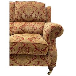 Parker Knoll - three-seat 'Oakham' hardwood-framed sofa, upholstered in red and gold floral pattern fabric, on turned feet with brass cups and castors 