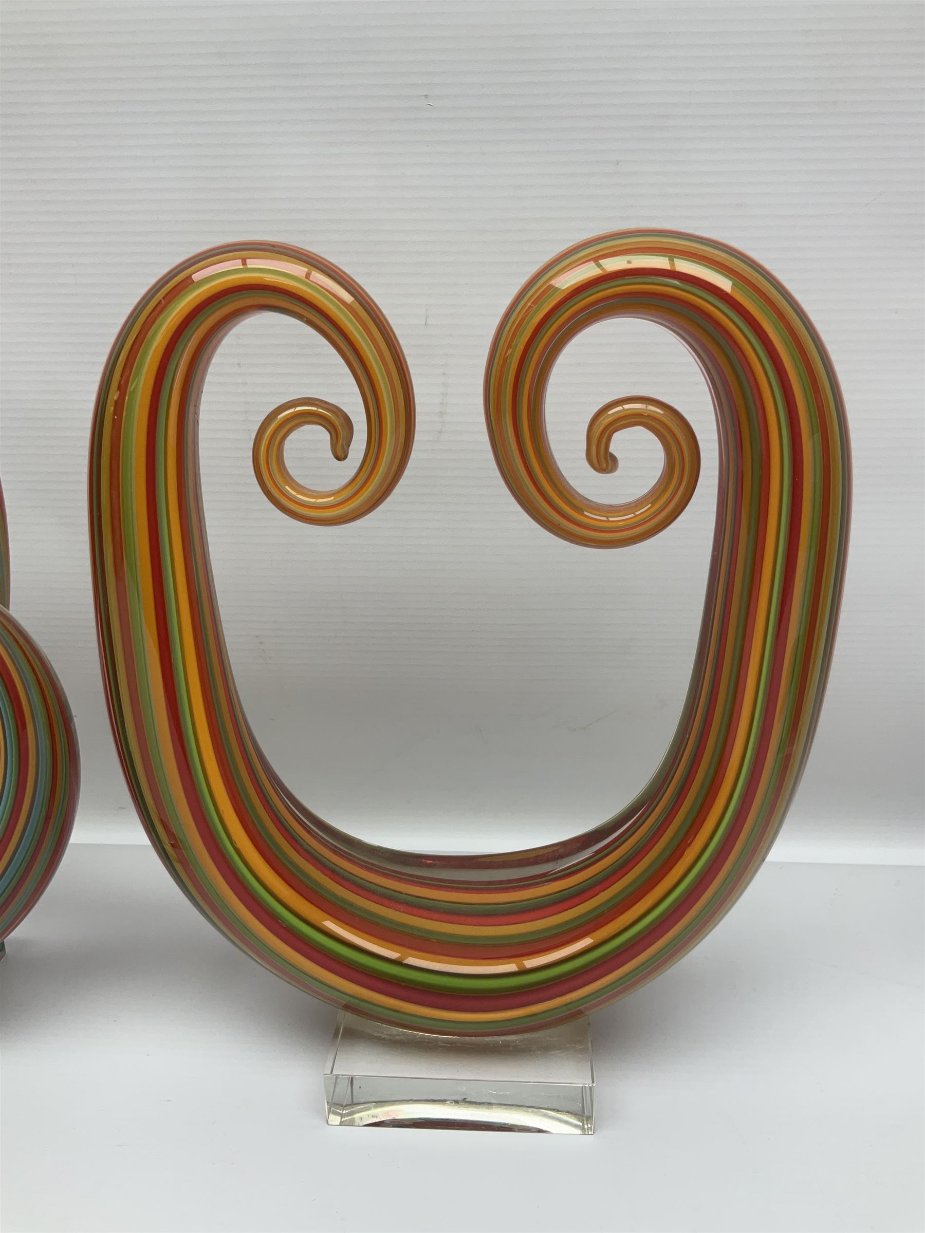 Three art glass sculpture, coiled form with multicolour stranded, upon clear glass plinth, unsigned, largest H27cm