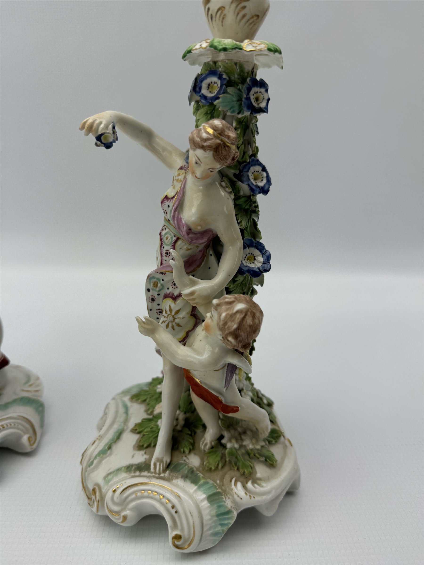 Pair of Derby figural candlesticks, modelled as Venus & Cupid and Mars, Mars wears armour with a shield to his right, Venus dressed in a robe with floral decoration and Cupid by her side, both with pierced sconces above bocage stems, on scrolling raised bases, unmarked, H27cm max (2)