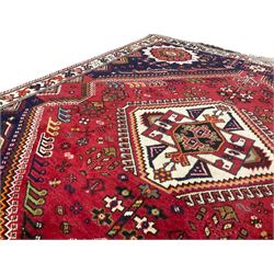 Persian Quashqai crimson ground rug, central geometric lozenge medallion surrounded by stylised plant motifs, indigo spandrels with further geometric designs, enclosed by an ivory border