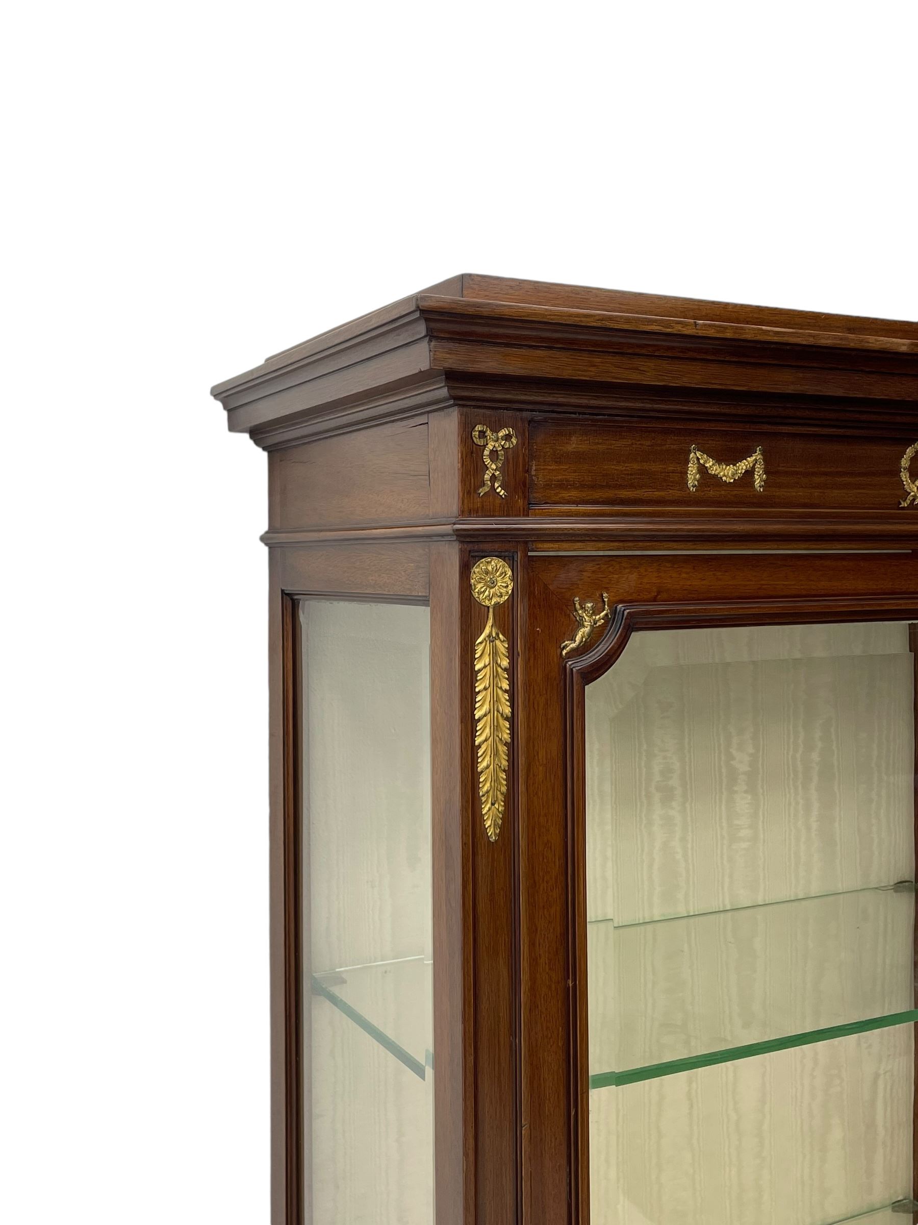 Early 20th century Louis XVI design mahogany vitrine display cabinet, projecting stepped cornice over recessed frieze decorated with gilt metal mounts of festoons and a bellflower wreath, fabric lined interior with two glass shelves, enclosed by bevel glazed door with lower panel, on two turned front feet 