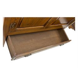 Oak drinks or media cabinet, projecting moulded cornice over two Gothic arch panelled doors on sliding tracks enclosing open storage, two drawers with brass drop handles, on bracket supports