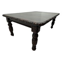 19th century heavily carved oak extending dining table, rectangular top with rounded corners and carved gadrooned edge, extending via winding mechanism with two additional leaves, raised on acanthus leaf-carved baluster supports terminating in ceramic castors