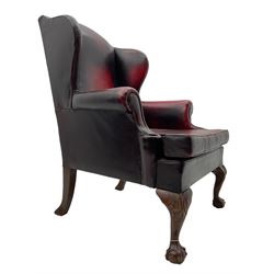 Georgian design hardwood-framed wingback armchair, upholstered in red leather, loose seat cushion and rolled arms, on acanthus carved ball and claw front feet 