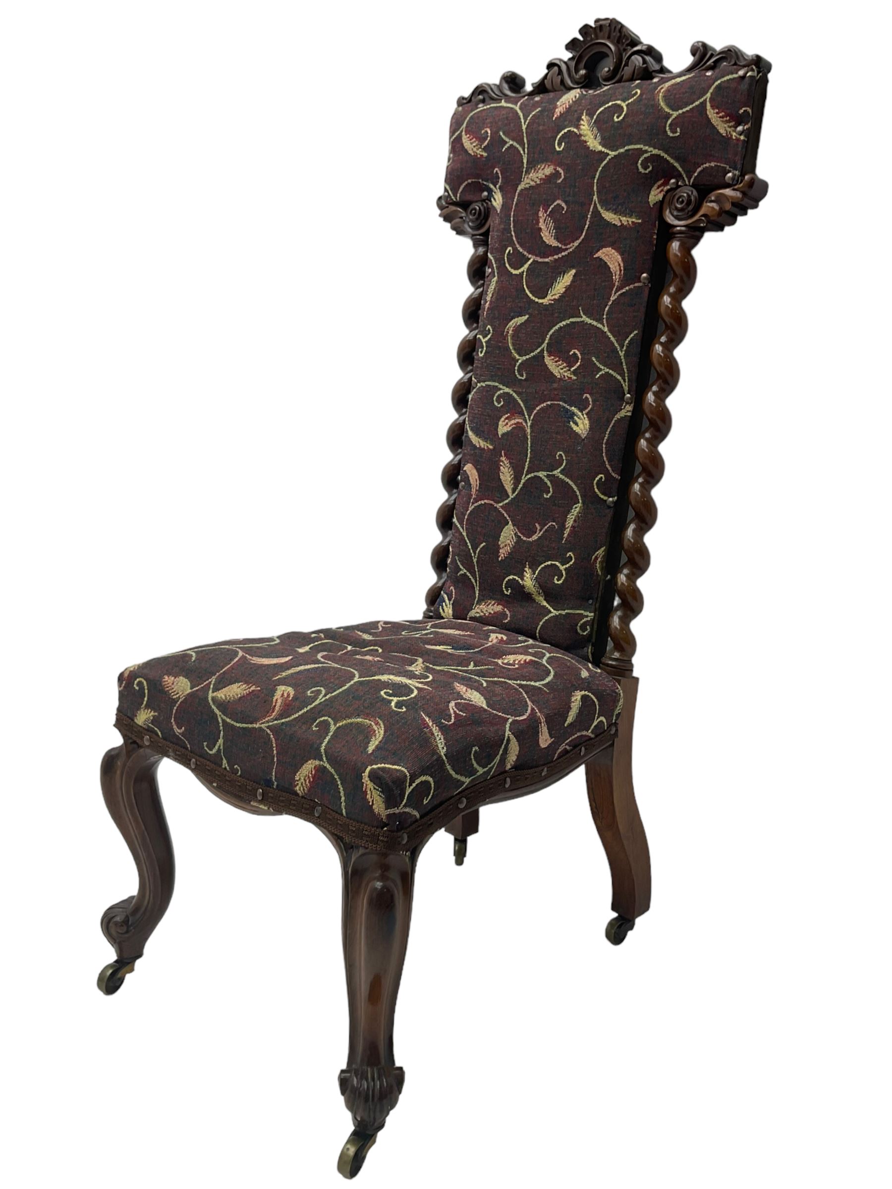 Victorian walnut prie-dieu chair, cresting rail carved with cartouche and extending scrolling foliage, back flanked by spiral turned column uprights, upholstered in foliate patterned fabric, raised on cabriole supports with scroll feet and castors