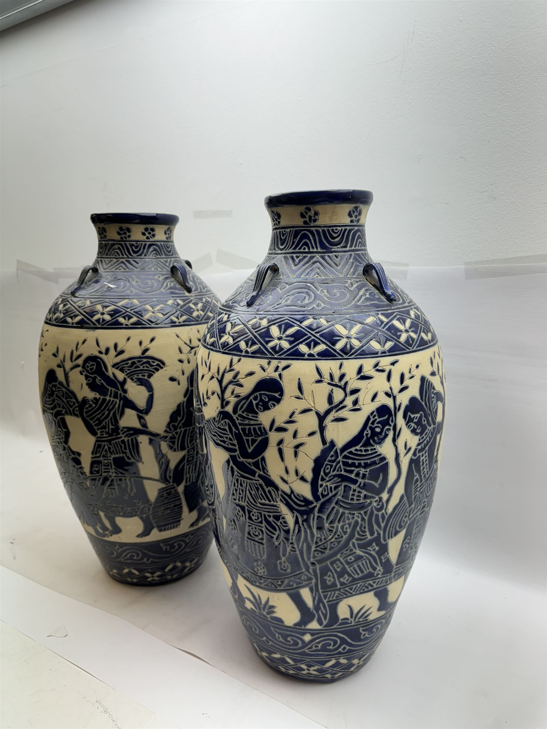 Pair of blue and white Cretan style vases, decorated with figures among trees with blue boarders on a white ground, H55cm