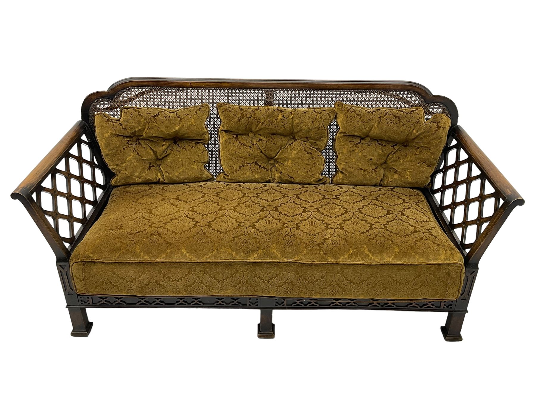 Early 20th century three-piece bergère suite - three seat sofa (W177cm, H82cm, D75cm); pair of matching armchairs (W84cm); single caned back with 'cock-pen' panelled arms, upholstered in foliate pattern fabric, blind fretwork lower frieze over square feet 