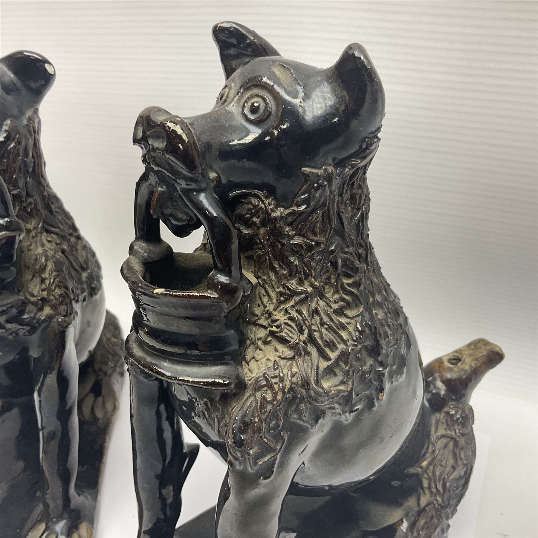 Pair of unusual early English pottery figures, modelled in the form of seated dogs with baskets between their jaws, the tails forming whistles, each upon rectangular base, overall H22cm