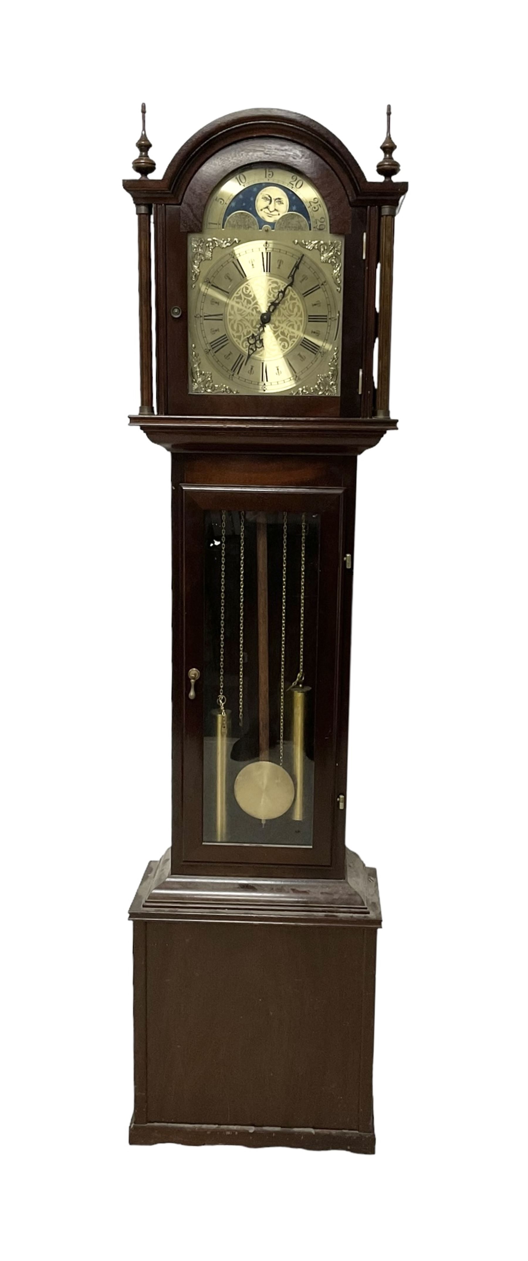 20th century - Westminster chime 8-day grandmother clock in a mahogany case, with a break arch top and brass finials, fully glazed trunk door with visible brass cased weights and pendulum, brass dial with etched dial centre and spandrels, chapter ring with Roman numerals and working moon disc to the arch, two train chain driven movement with 12 gong rods and chime selection for the quarters and hours.