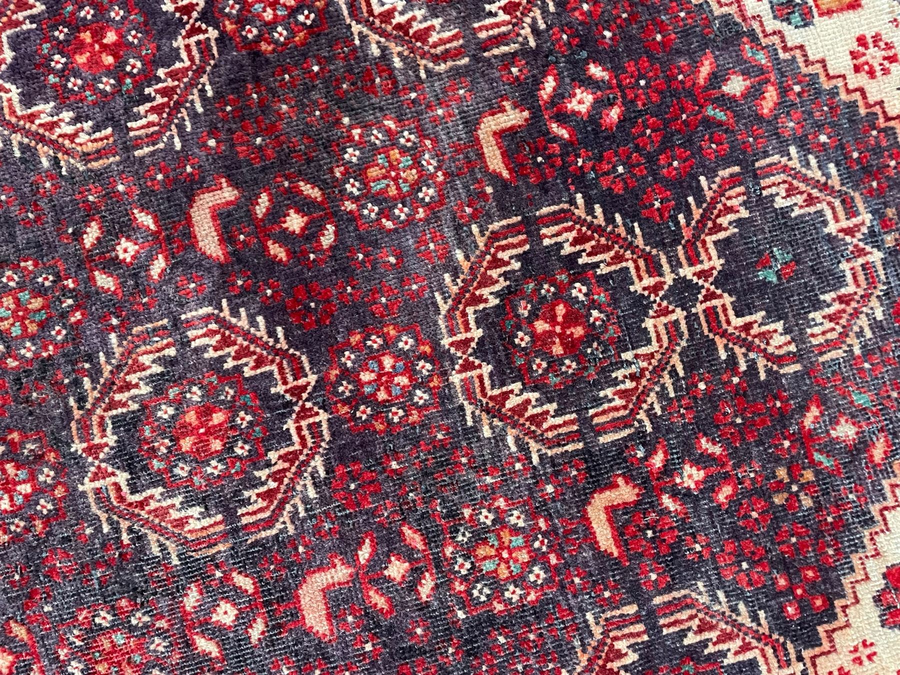 Persian Baluchi dark indigo and crimson ground rug, the field decorated with rows of repeating Pitrak motifs and surrounded by small bird and flower head motifs, floral urn decorated spandrels, repeating Pitrak border within guard stripes