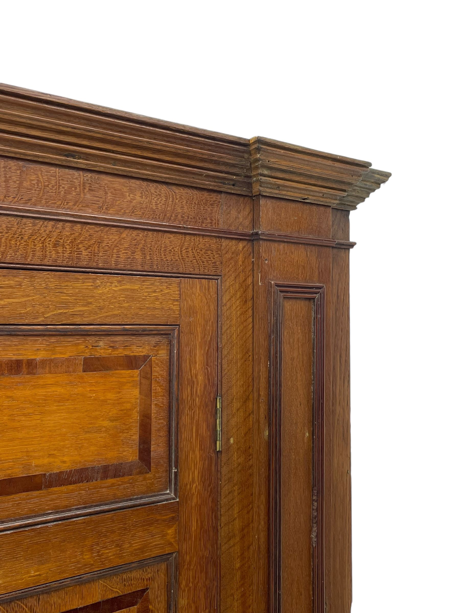 George III and later oak and mahogany banded corner cupboard, moulded cornice over four panelled doors, the door panels inlaid with mahogany bands, projecting square pilasters throughout with applied reeded mouldings, the painted interior fitted with shaped shelves, on moulded plinth base 