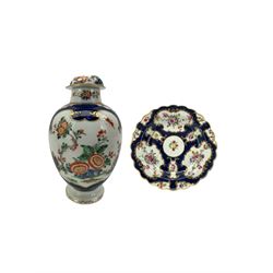 18th century Worcester tea caddy, of oval form and painted in the Kakiemon palette with reserves of flowers against a blue scale ground, H14cm together with a similar Worcester circular dish, painted with floral sprays, within a scalloped edge, blue crescent mark beneath, D19cm (2)