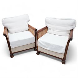 Pair of early 20th century mahogany framed bergère armchairs, upholstered back and seat flanked by rolled double-caned arms with carved scale decoration, floral and ribbon-twist carved lower edge, over ball-and-claw feet