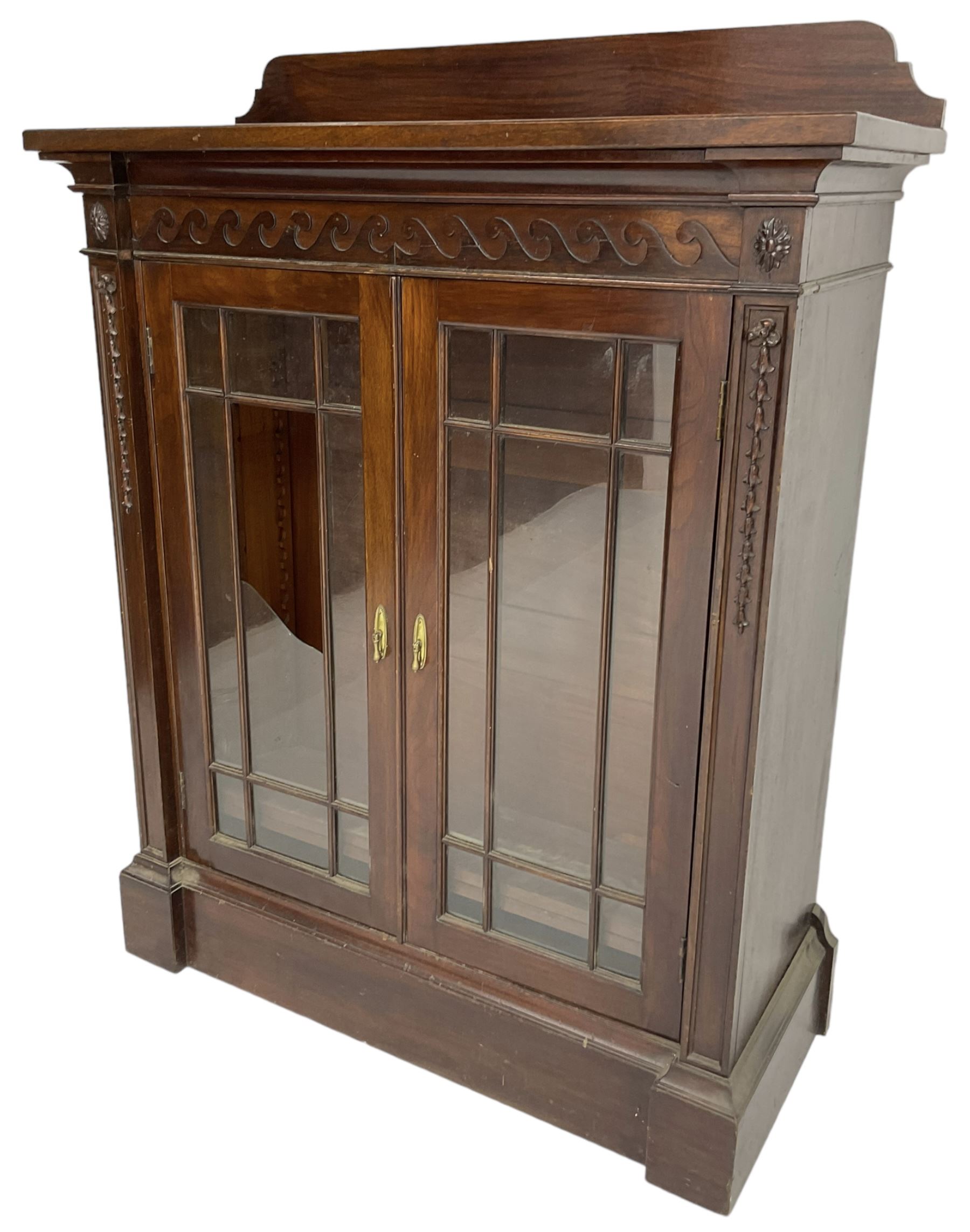 19th century mahogany display cabinet, rectangular top over frieze decorated with Vitruvian scroll mount, enclosed by two astragal glazed doors, the upright rails decorated with trailing bellflowers, on moulded plinth