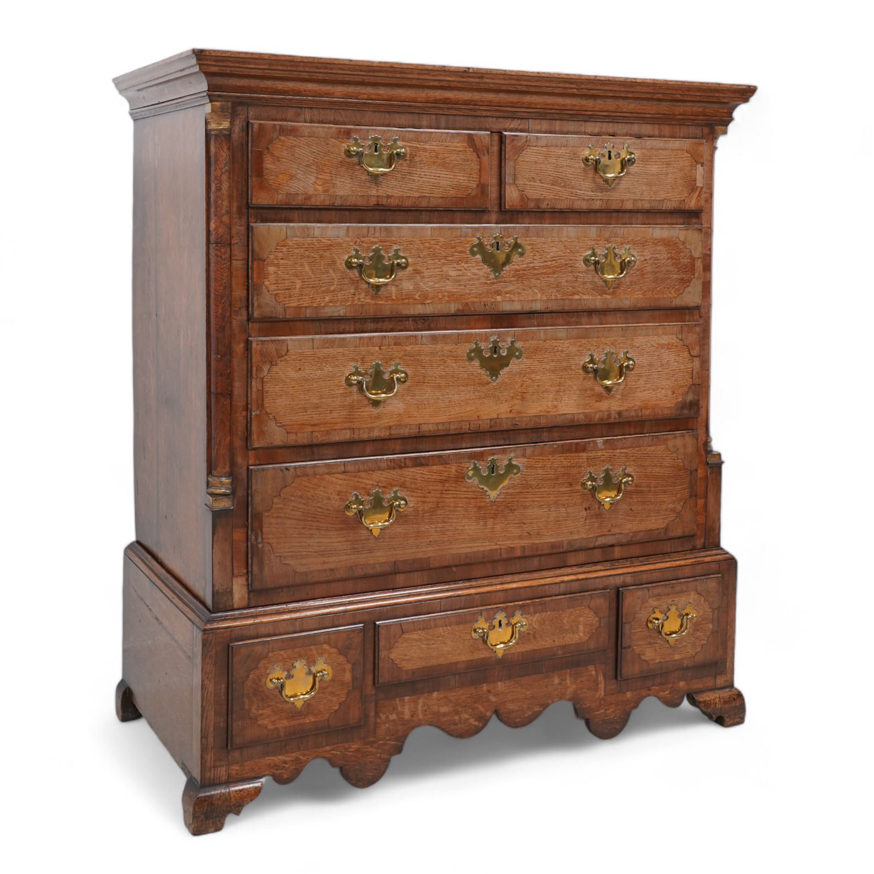 George III oak and mahogany banded chest on stand, moulded cornice over two short and three long drawers, shaped brass handle plates and swan neck handles, enclosed by canted corners with turned quarter columns, the stand fitted with three drawers, on bracket feet