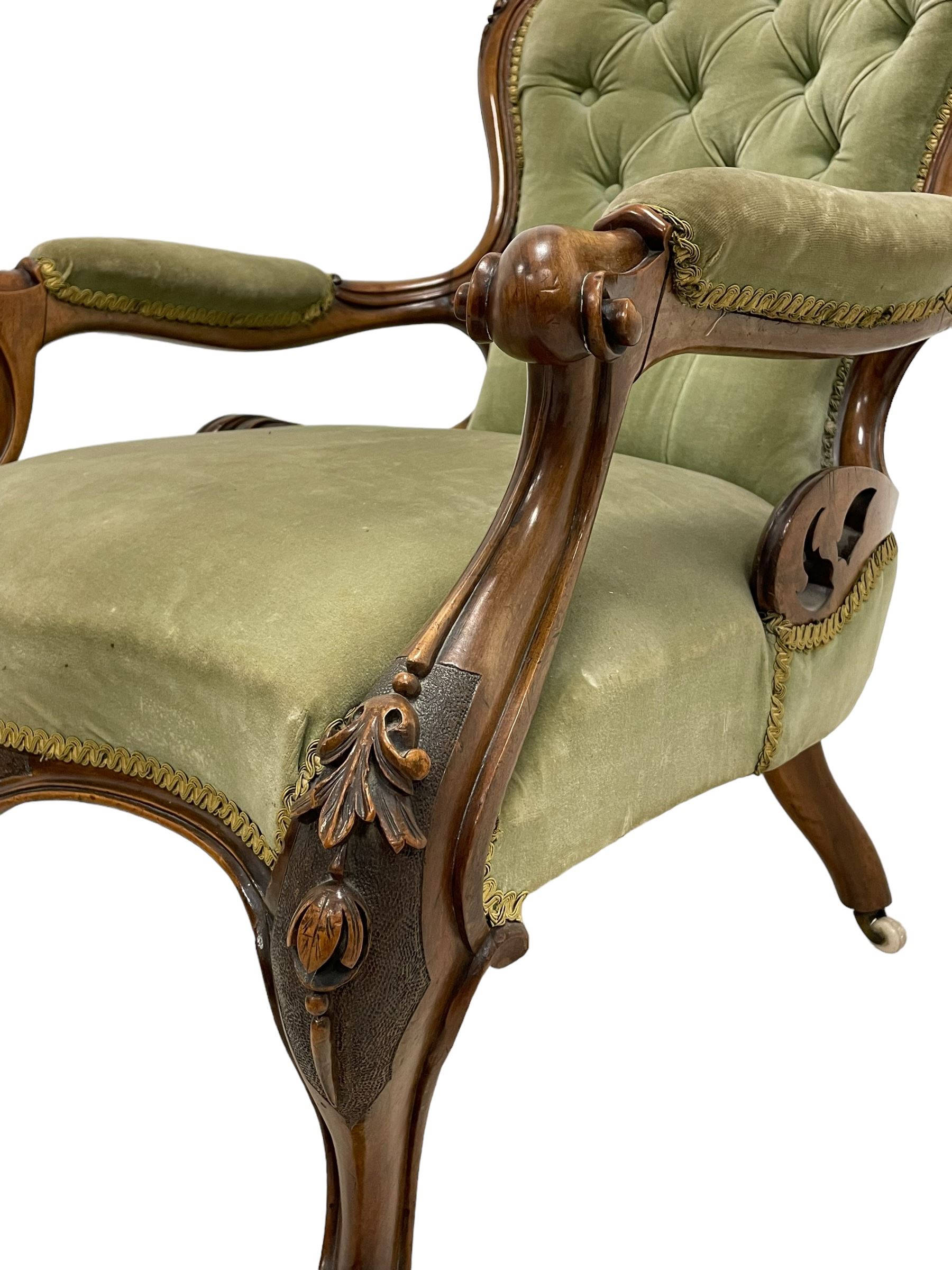 Pair of lady's and gentleman's Victorian carved walnut armchair and nursing chair, foliate carved cresting rail over shaped back with scrolled acanthus carved sides, the armchair with scroll arm terminals, the spoon back and sprung seat upholstered in buttoned sage green velvet, raised on cabriole supports with bell-flower moulded knees and scroll feet, on ceramic castors