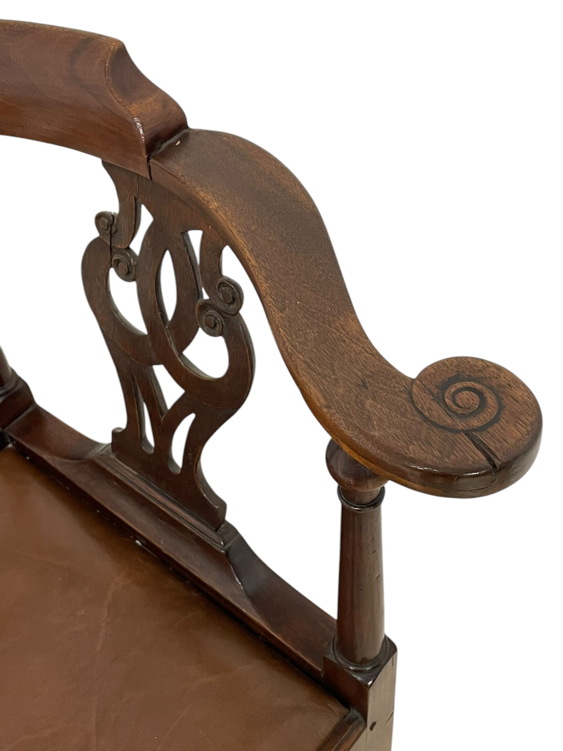 George III mahogany corner elbow chair, curved back rest and shaped arms with scroll carved terminals, on turned supports and pierced scroll carved interlaced splats, drop-in seat upholstered in brown leather, on square supports with inner chamfer and outer moulding 