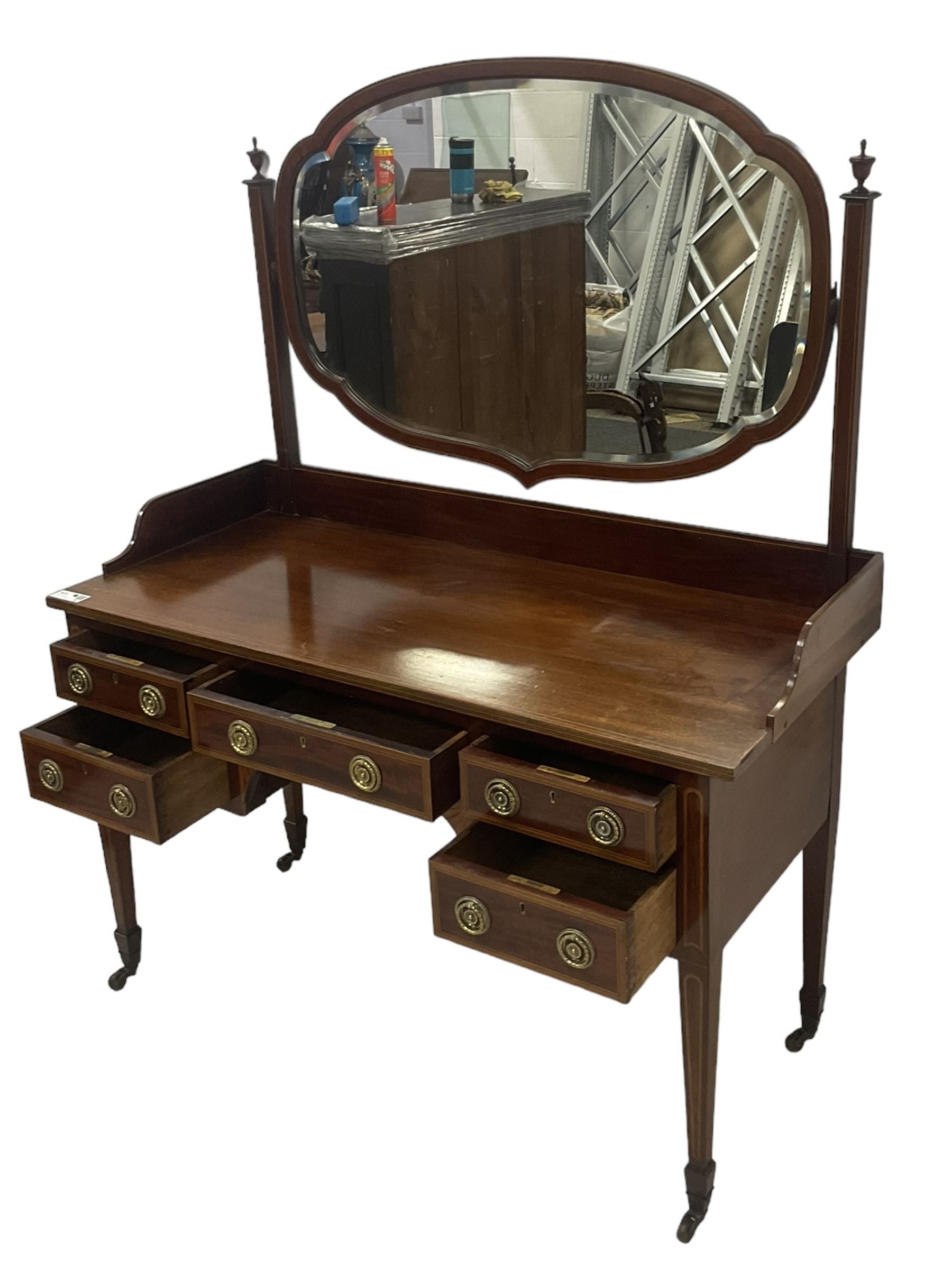 Edwardian inlaid mahogany kneehole dressing table, raised shaped oval bevelled mirror back, fitted with five drawers with banding and stringing, on square tapering supports with castors