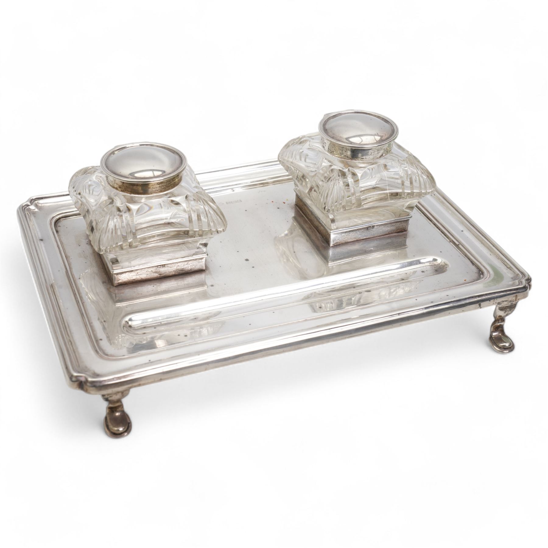 George V silver inkstand of rectangular design with pen tray and two cushion shape glass inkwells with silver covers, raised edge and four shaped supports 28cm x 20cm Birmingham 1912 Maker William Hutton & Sons