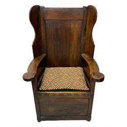 George III oak lambing chair, tall rectangular panelled backrest with shaped wings over broad scrolled armrests, box seat with removable geometric upholstered cushion, integrated drawer to lower section, resting on square supports