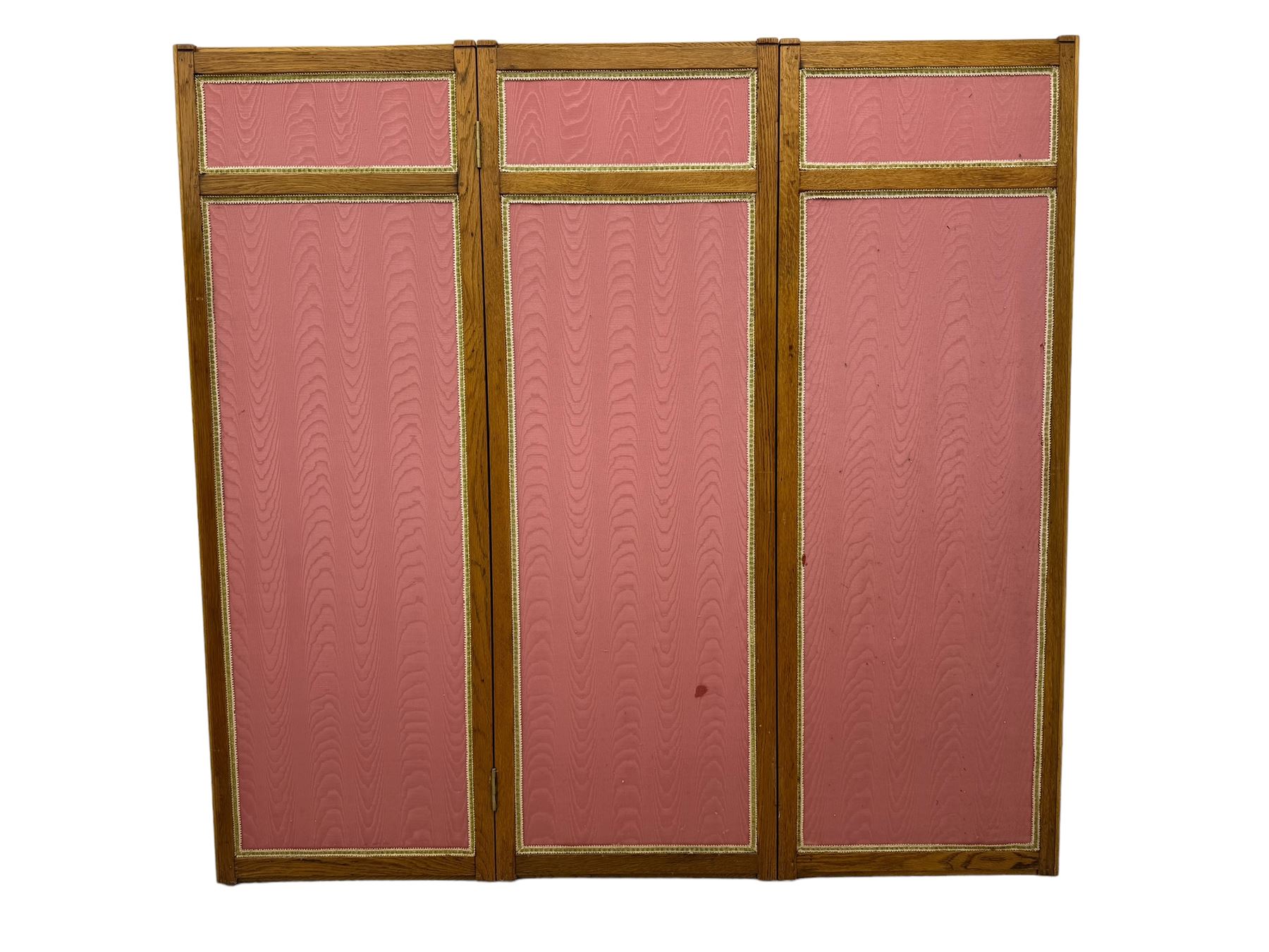 Edwardian oak and fabric folding screen, featuring three panels with oak frames, one side covered in green striped fabric with decorative trim, the reverse side in pink moiré effect fabric, connected by brass hinges