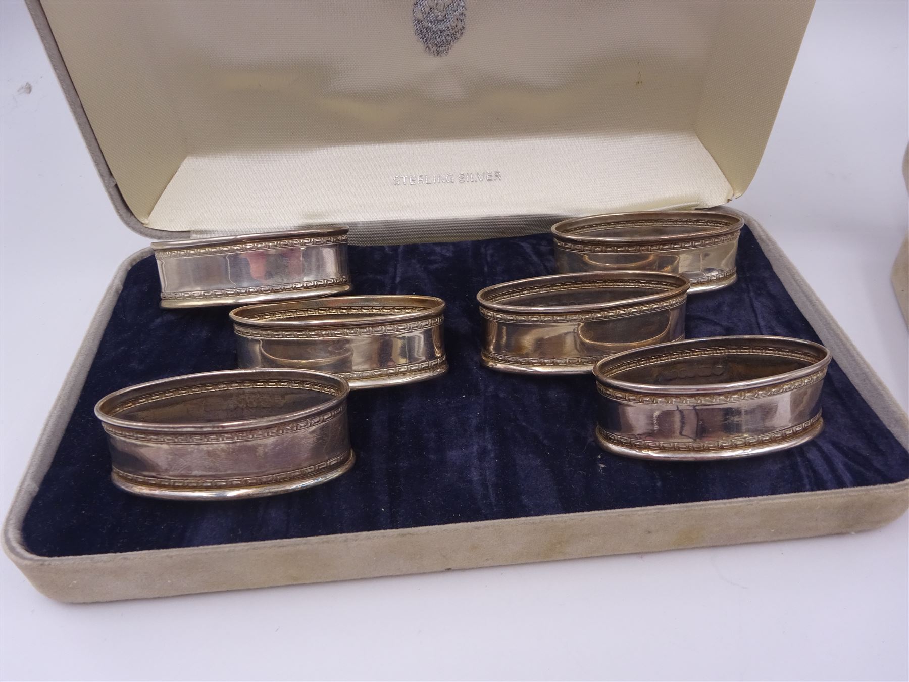 Two sets of six modern silver napkin rings, each of oval form, with Greek key decoration, hallmarked Ari D Norman, London 1986, both in fitted cases