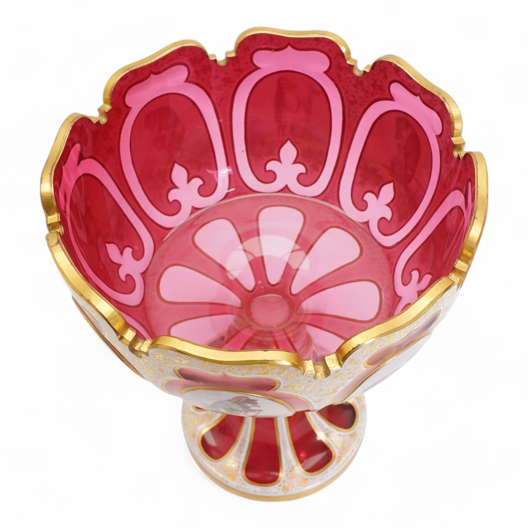 Late 19th century Bohemian white overlaid cranberry glass pedestal bowl, with fancy scalloped rim and cut with oval and fleur de lis shaped panels, each enamelled with 'Reynard the Fox' anthropomorphic animals, after the illustrations by Wiilhem Von Kaulbach,  within gold borders with gilt scrolling decoration, supported by a slice cut circular spreading foot with further gilt decoration, H28.5cm x W22.5cm