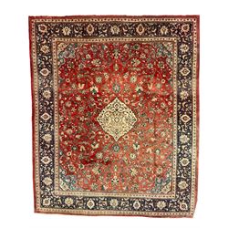 Persian Kashan crimson ground carpet, central shaped pale ground medallion surrounded by interlacing branches and stylised floral motifs, indigo main border with scrolling foliage design, within guard stripes 