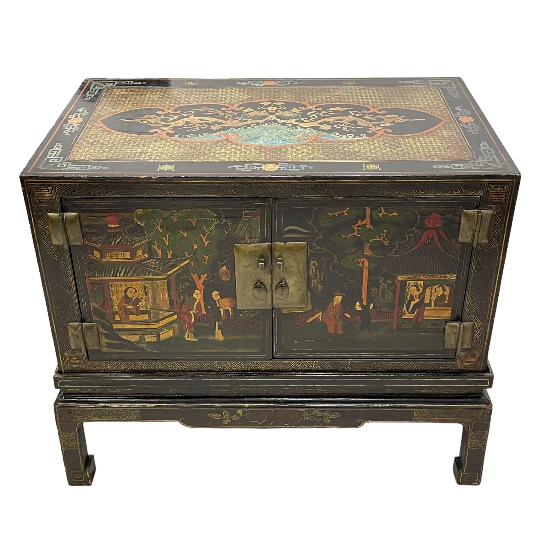 Pair of early 20th century Chinese ebonised and lacquered wood cabinets, the top decorated with dragons over lapping waves within a gilt patterned panel, the surrounding band decorated with Chinese symbols and flowerheads, enclosed by two doors each with village scenes with pagodas, figures and trees, the panelled sides decorated with a figure riding a dragon on stands with gilt decorated 