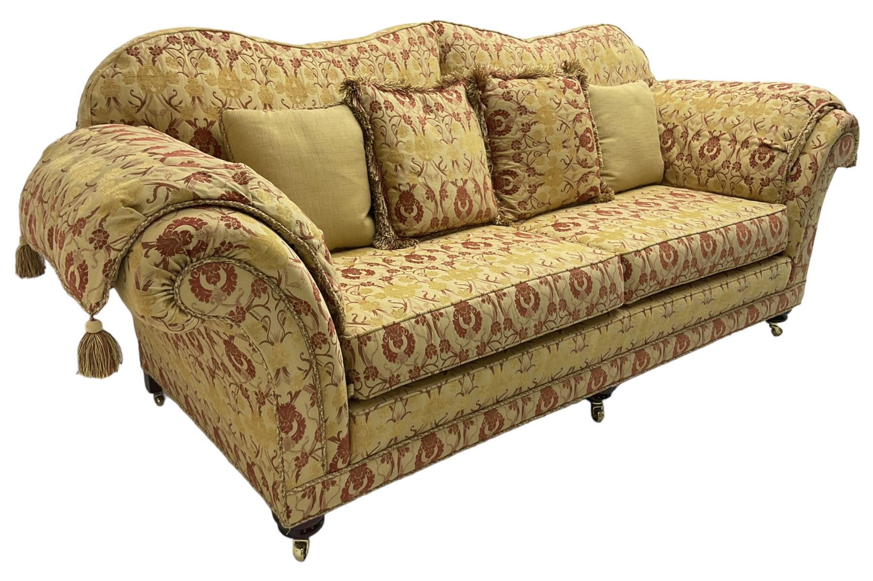 Steed Upholstery Ltd. - 'Lincoln' three-seat sofa upholstered in gold 'Olympia' floral pattern corded and tasselled fabric, together with scatter cushions and arm covers, on turned feet with brass castors