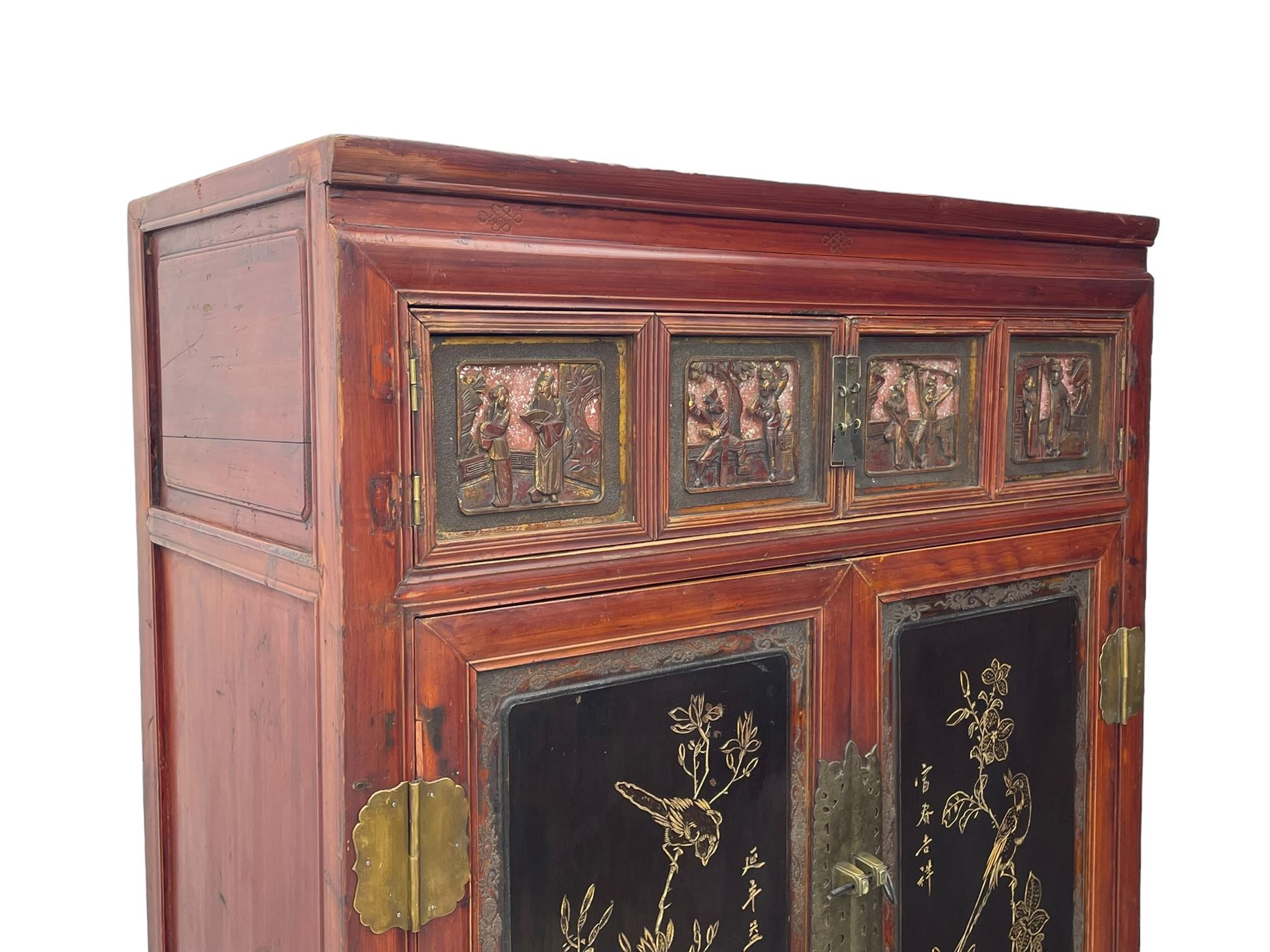 Late 19th century Chinese Qing dynasty red and black lacquered wood cabinet, Fujianese province, upper cupboard enclosed by two doors with relief carved and gilt panels depicting figures behind glass, the large cupboard enclosed by two panelled doors carved with trailing foliate branches and birds, inscribed with Chinese characters, to the left ‘Prolong life’ and to the right ‘Wealth and good fortune’, fitted with two drawers, square supports with carved brackets 