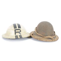 Two WWII British brodie helmets, one example painted white with a black R tot eh front and back, with neck strap  