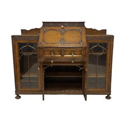 Early 20th century heavily carved oak bookcase bureau, raised back with grape-vine carved frieze, over fall-front enclosing fitted interior, above two short drawers and curved frieze drawer, flanked by astragal glazed and panelled cupboards, on turned feet