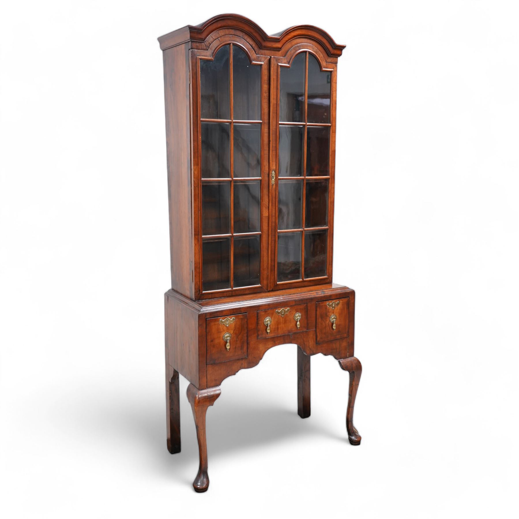 George II design walnut cabinet on stand, double arched top with applied mouldings over two astragal glazed doors, three internal shelves, the stand with moulded rectangular top fitted with three short drawers over shaped apron, on cabriole front supports 