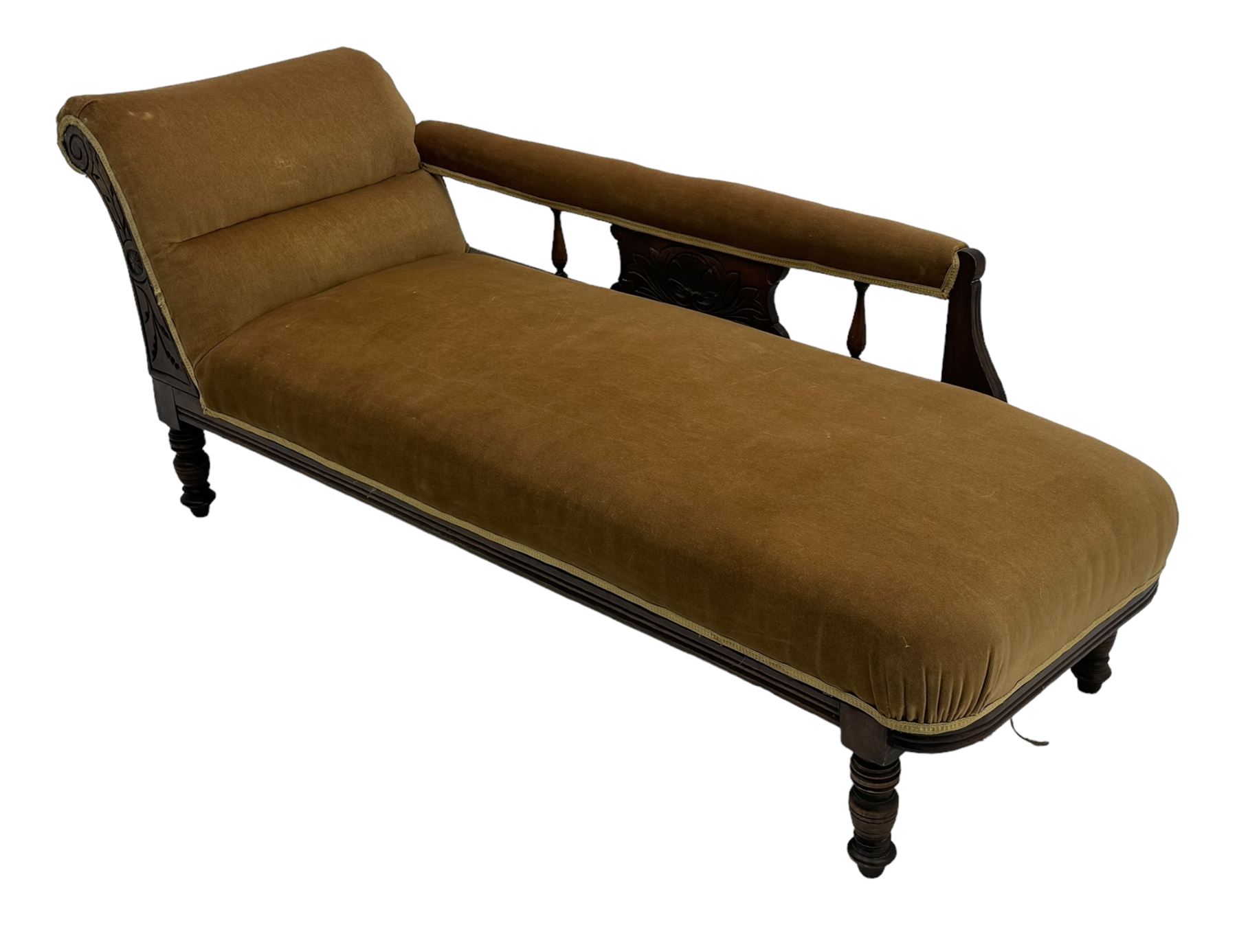 Late 19th century mahogany framed chaise longue, upholstered in tan fabric, featuring scrolled backrest with carved floral motifs, supported by turned legs