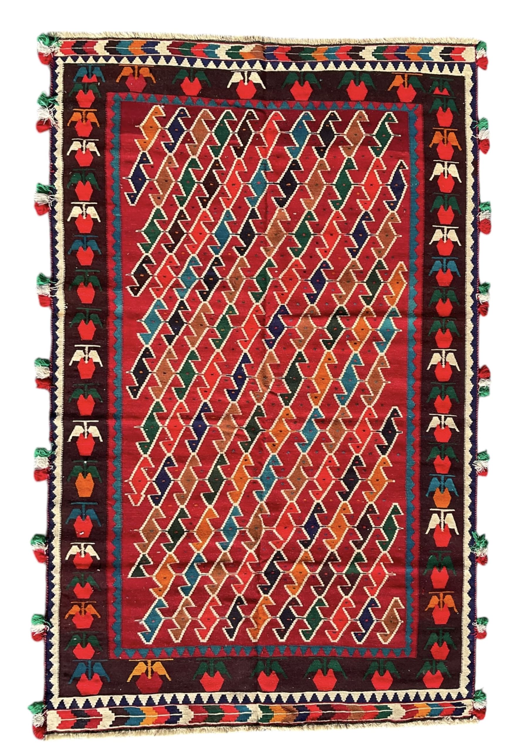 Southwest Persian Qashqai Kilim crimson ground rug, decorated with a repeating geometric pattern of interlocking diamond motifs in red, green, blue, and brown, enclosed by a deep brown border with stylised floral motifs and colourful fringe accents