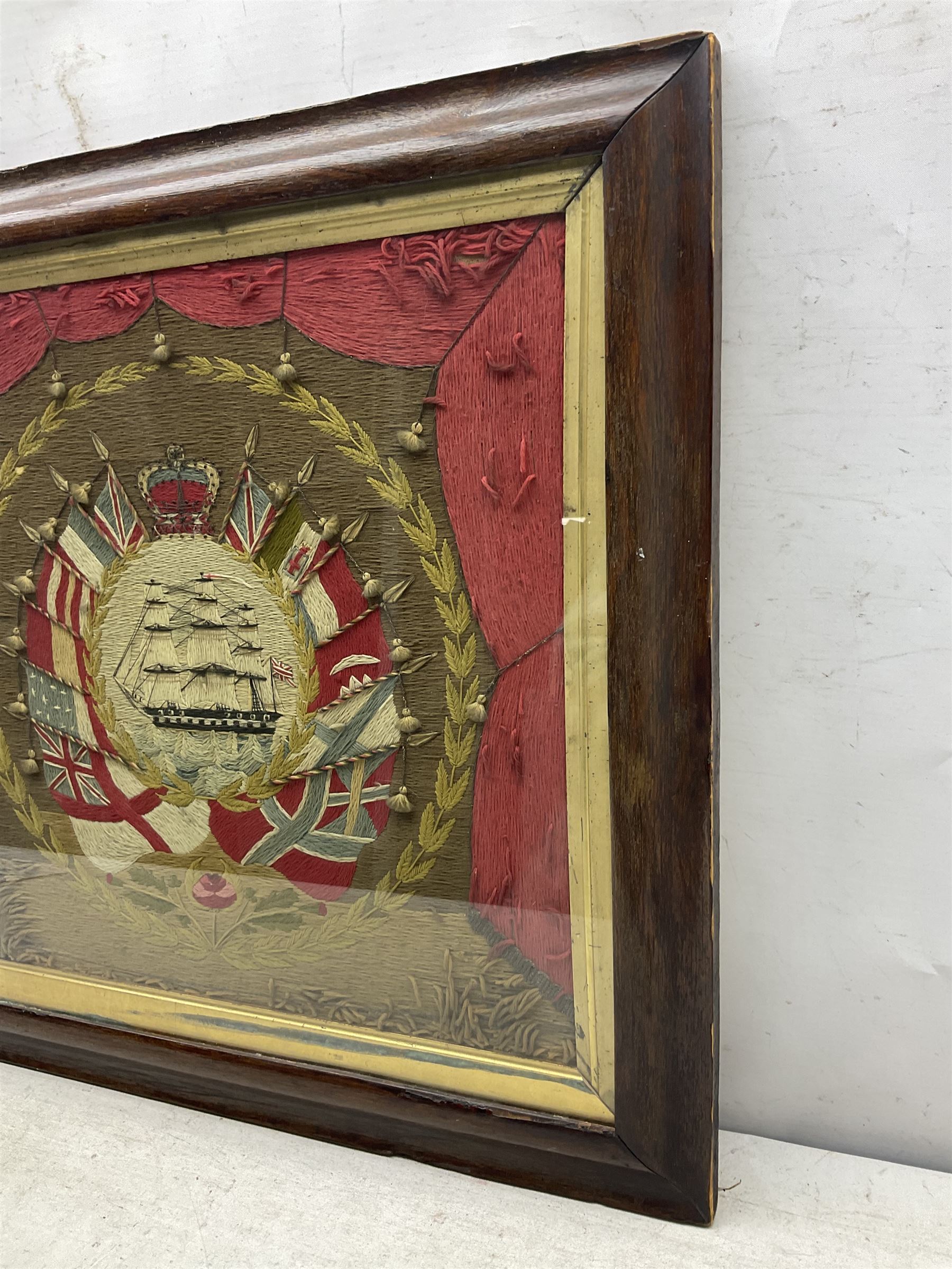 19th century woolwork, depicting a clipper ship, fully rigged over black hull with white ports, within a border of ensigns and flags and beaded crown above, in glazed wooden frame, H57cm