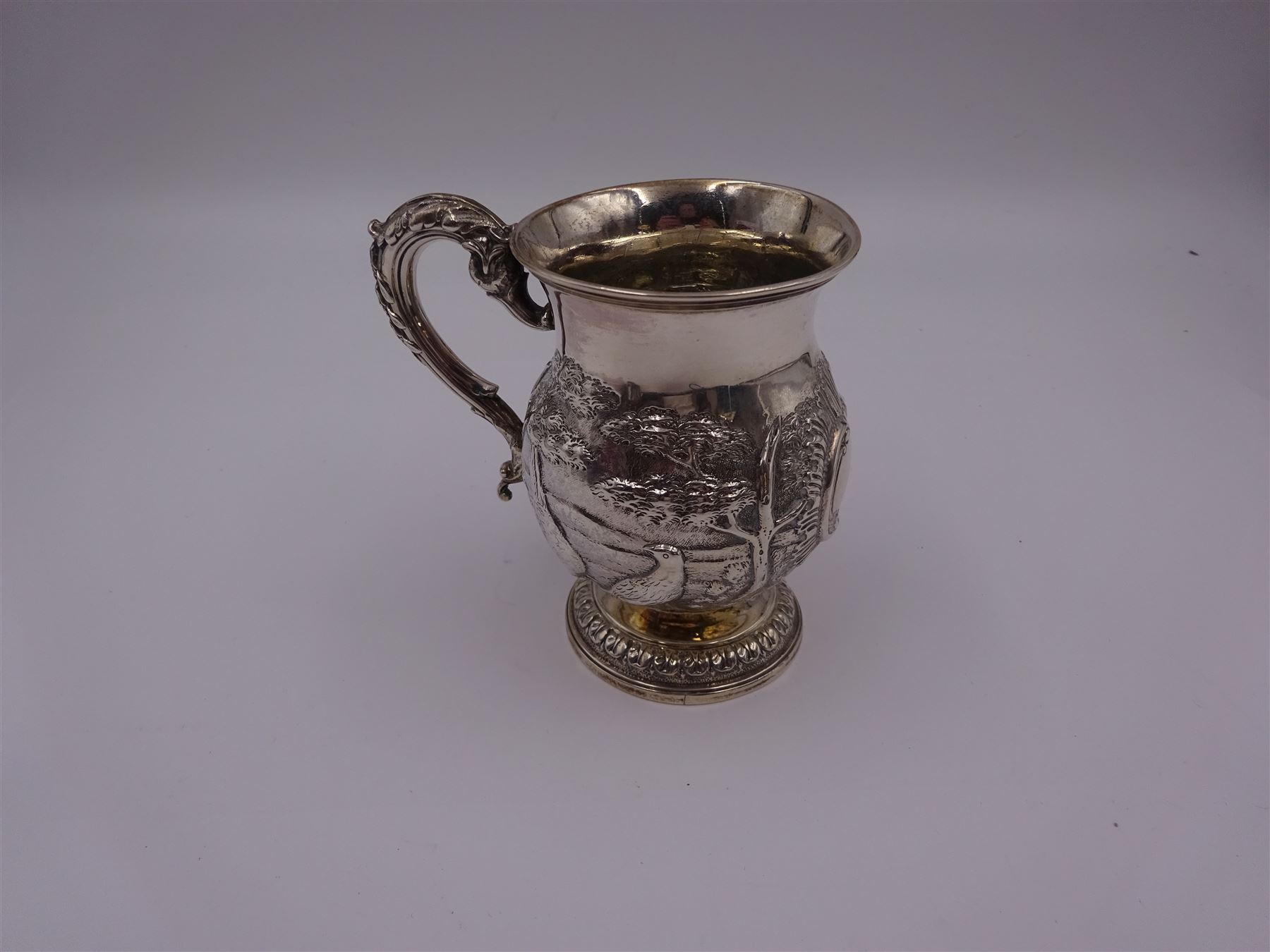 William IV silver christening mug, of waisted form, the body embossed with game birds in a countryside setting and a blank circular cartouche, with acanthus leaf capped scroll handle, upon a circular stepped foot, hallmarked Edward, Edward junior, John & William Barnard, London 1831, H10.2cm