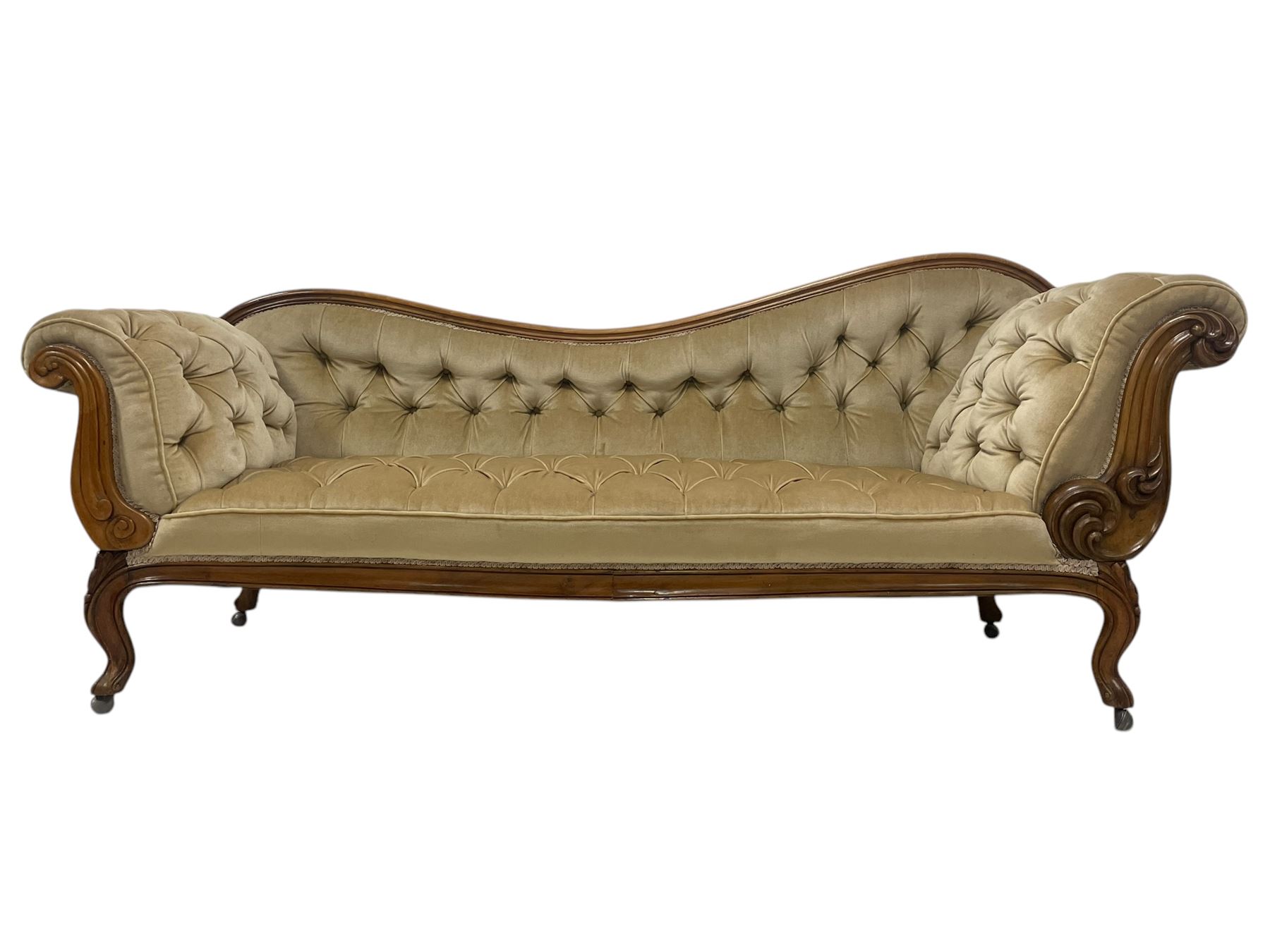 19th century walnut framed chaise longue, shaped back over scrolled arms decorated with moulded curling acanthus carvings, upholstered in deep buttoned champagne fabric, raised on cabriole supports with applied floral carved decoration, on castors