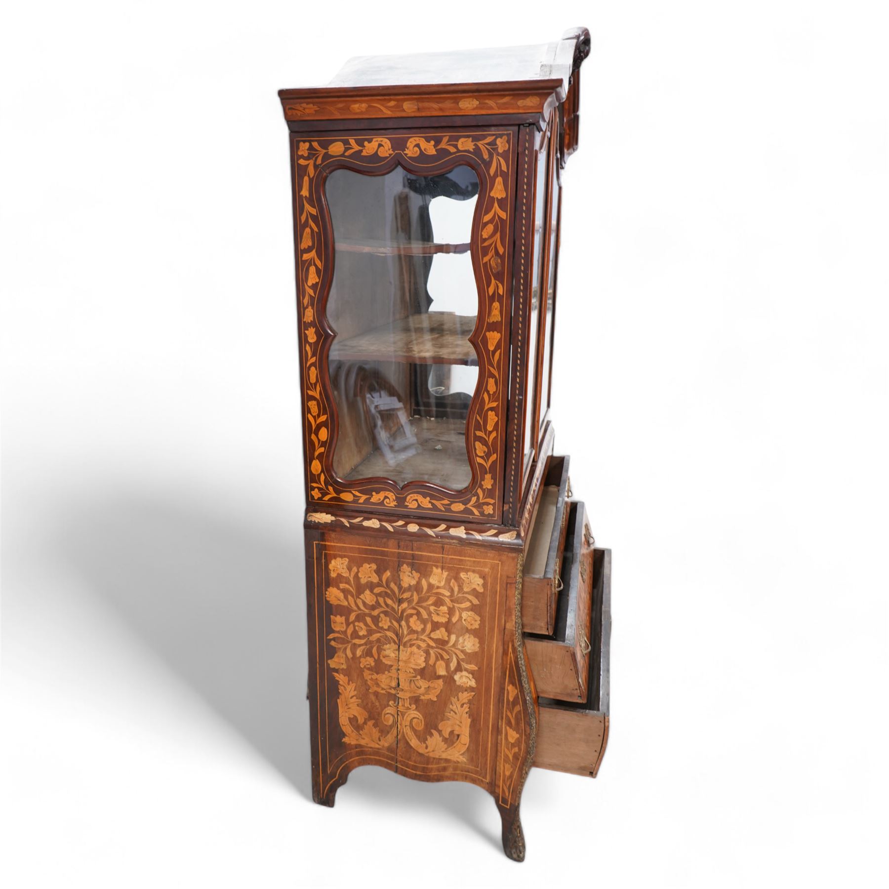 18th century Dutch marquetry walnut and gilt metal mounted vitrine cabinet on chest, shaped pediment carved with scrolling foliage cartouche, inlaid with trailing leafy branches and flower heads, two internal shelves enclosed by two glazed doors, the lower section with bombe outline fitted with three drawers, with ornate cast gilt metal edging and terminal caps