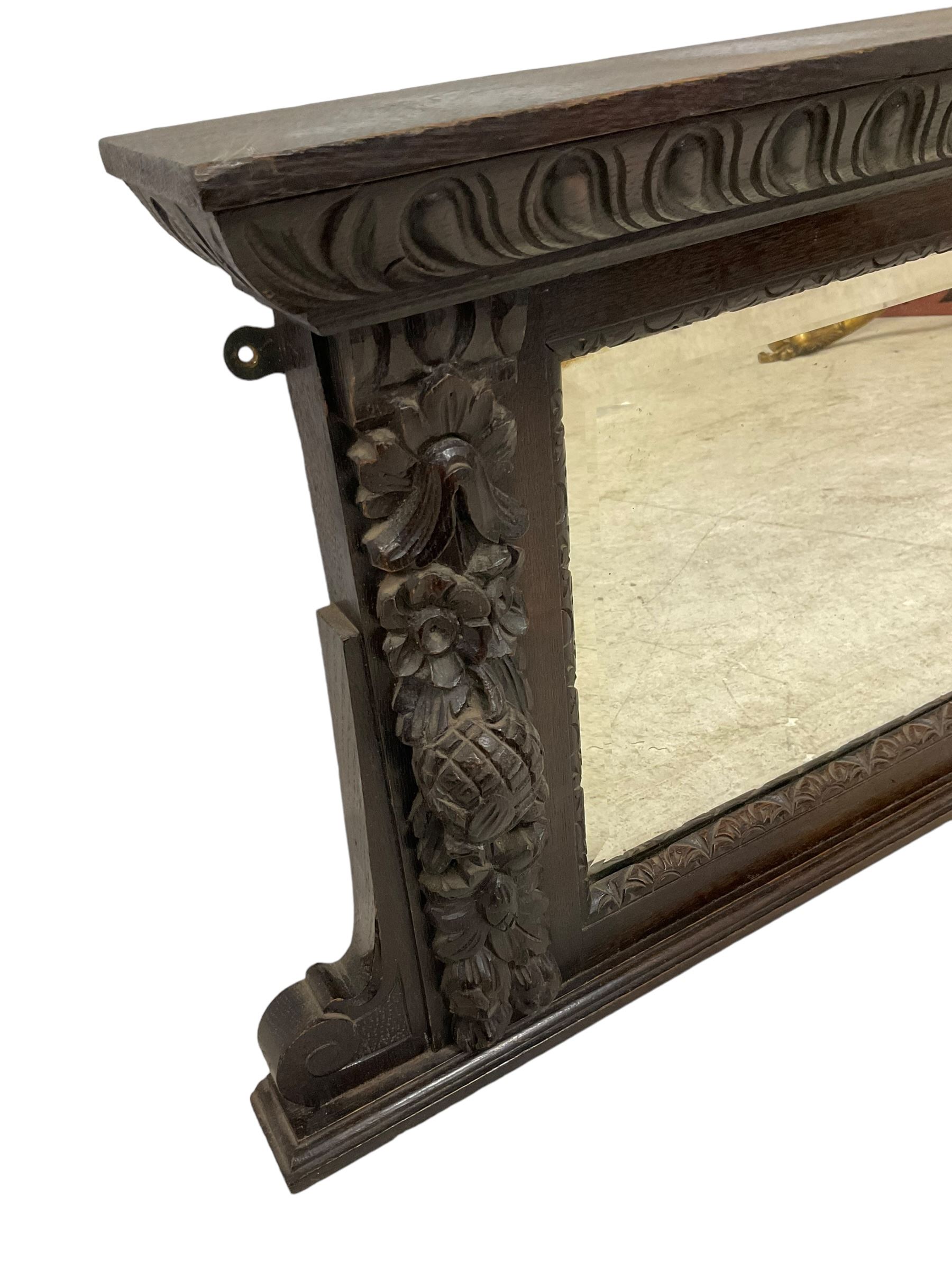 Victorian heavily carved oak wall mirror, projecting gadroon carved ovolo cornice, bevelled mirror plate within a lunette carved frame, decorated with applied fruit and foliage carved mounts, scroll carved brackets 