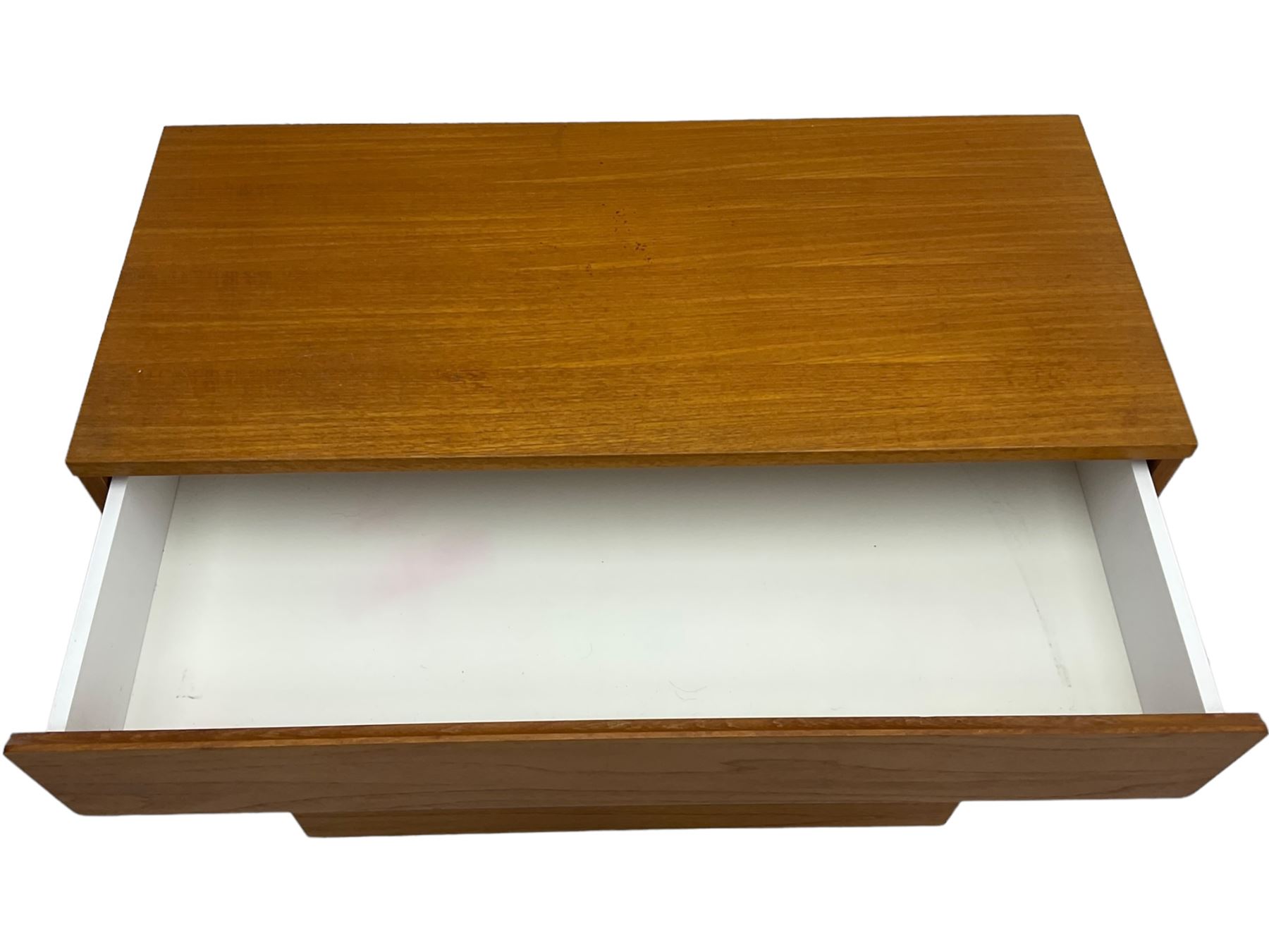 Mid-20th century teak four-drawer chest, featuring a minimalist design with two shallow and two deep flush drawer fronts, each with recessed handles along the top edge, the drawers open to reveal white laminate interiors, supported by castors