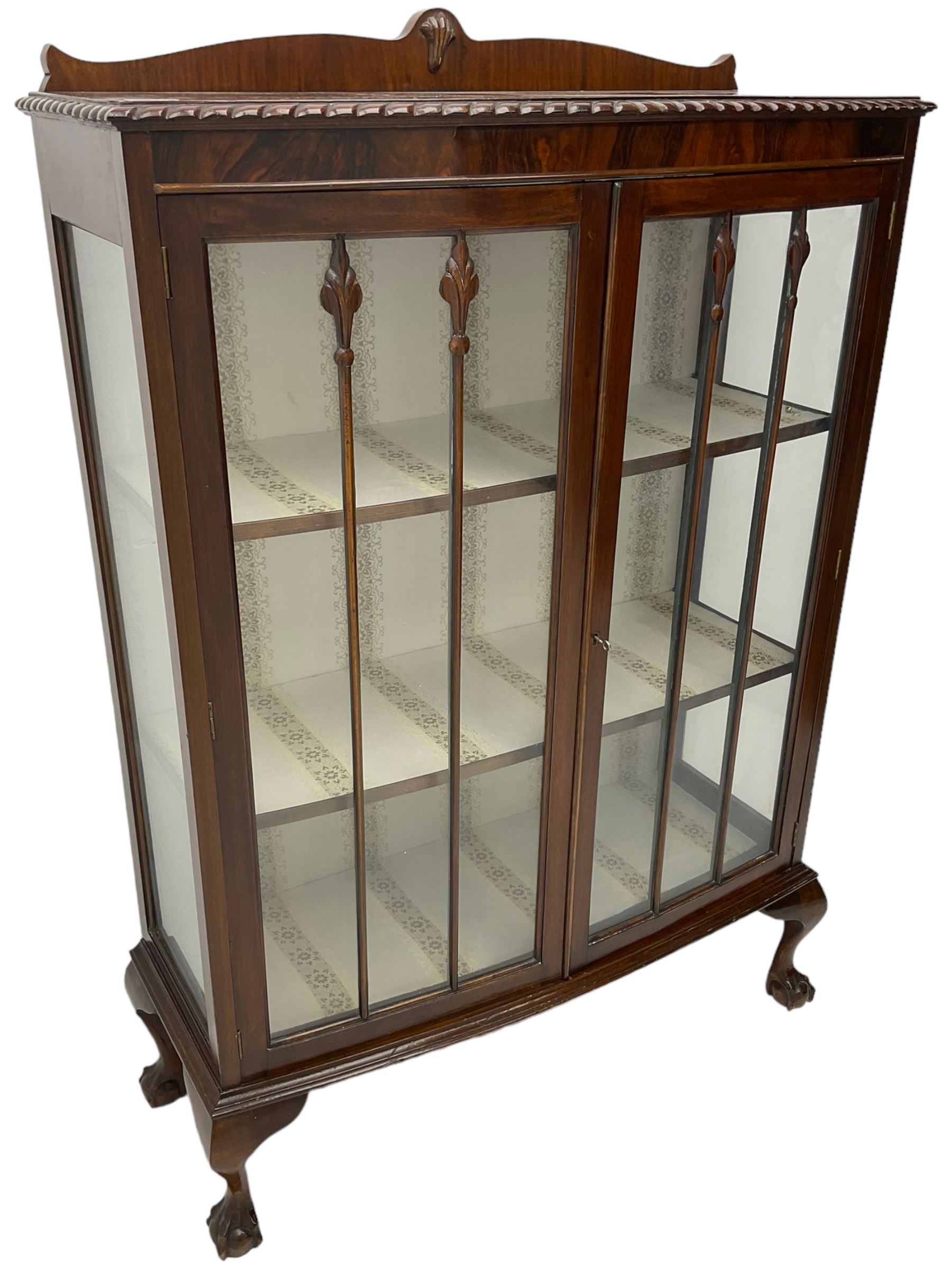 Early 20th century figured walnut bow-front display cabinet, enclosed by two glazed doors, on ball and claw cabriole feet