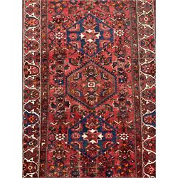 Persian Hamadan rug, red ground with overall geometric design, the field with three extended lozenges, decorated with geometric and stylised flower head motifs, the border and guards decorated with repeating geometric motifs