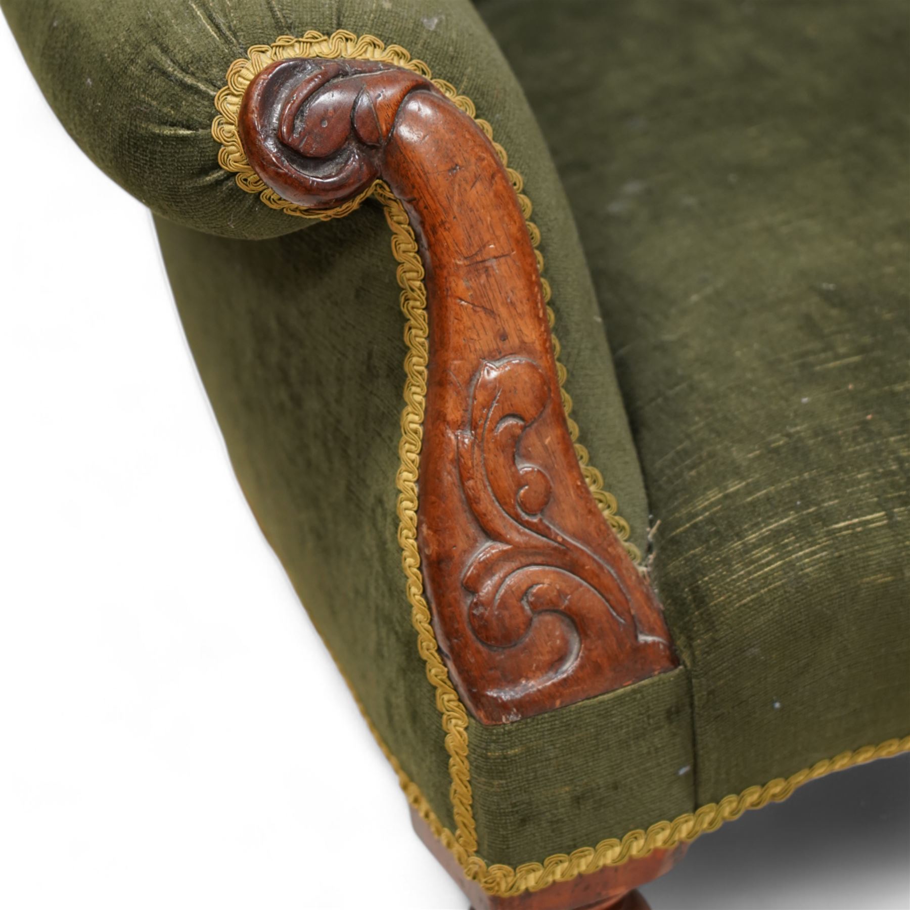 Victorian mahogany spoonback armchair, moulded frame with scroll carved terminals, upholstered in buttoned green fabric, rolled arms with foliage scroll carved facias, on turned front feet with brass cups and castors 