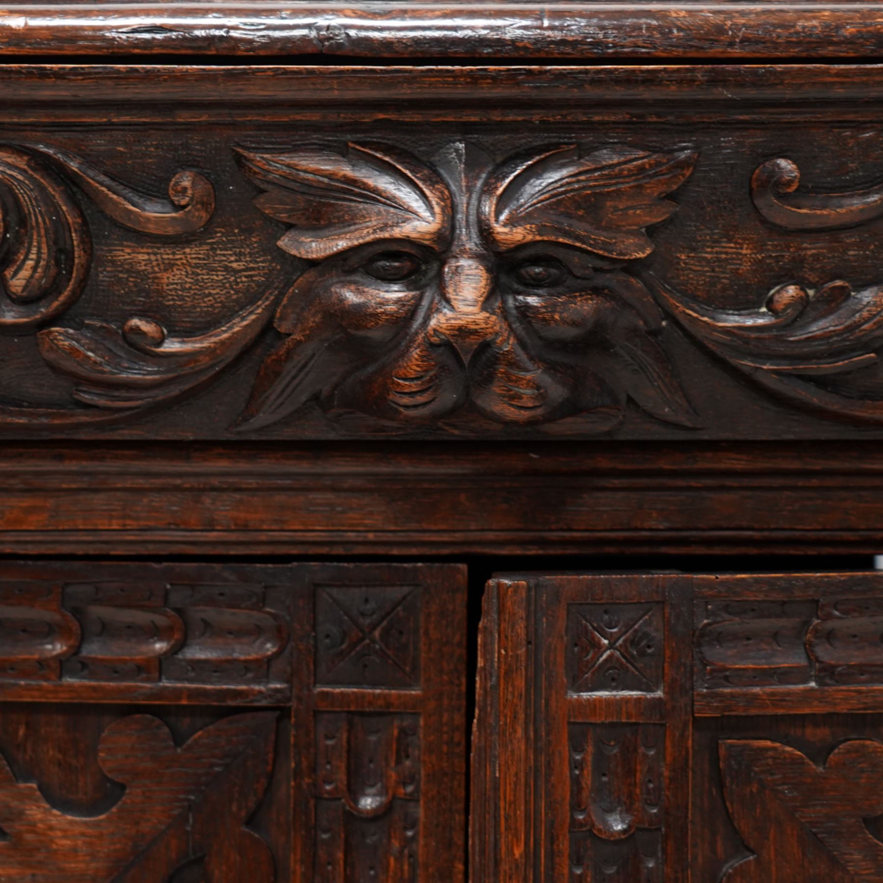 19th century Jacobean Revival heavily carved oak side cabinet, rectangular top with moulded edge, the frieze drawer applied with a central green man carved handle and surrounded scrolled acanthus leaves, over two panelled cupboards with egg-and-dart and rosette motifs with central lion mask mounts, flanked by uprights with further lion masks over protruding fruit and floral vines, lower moulded edge on square feet