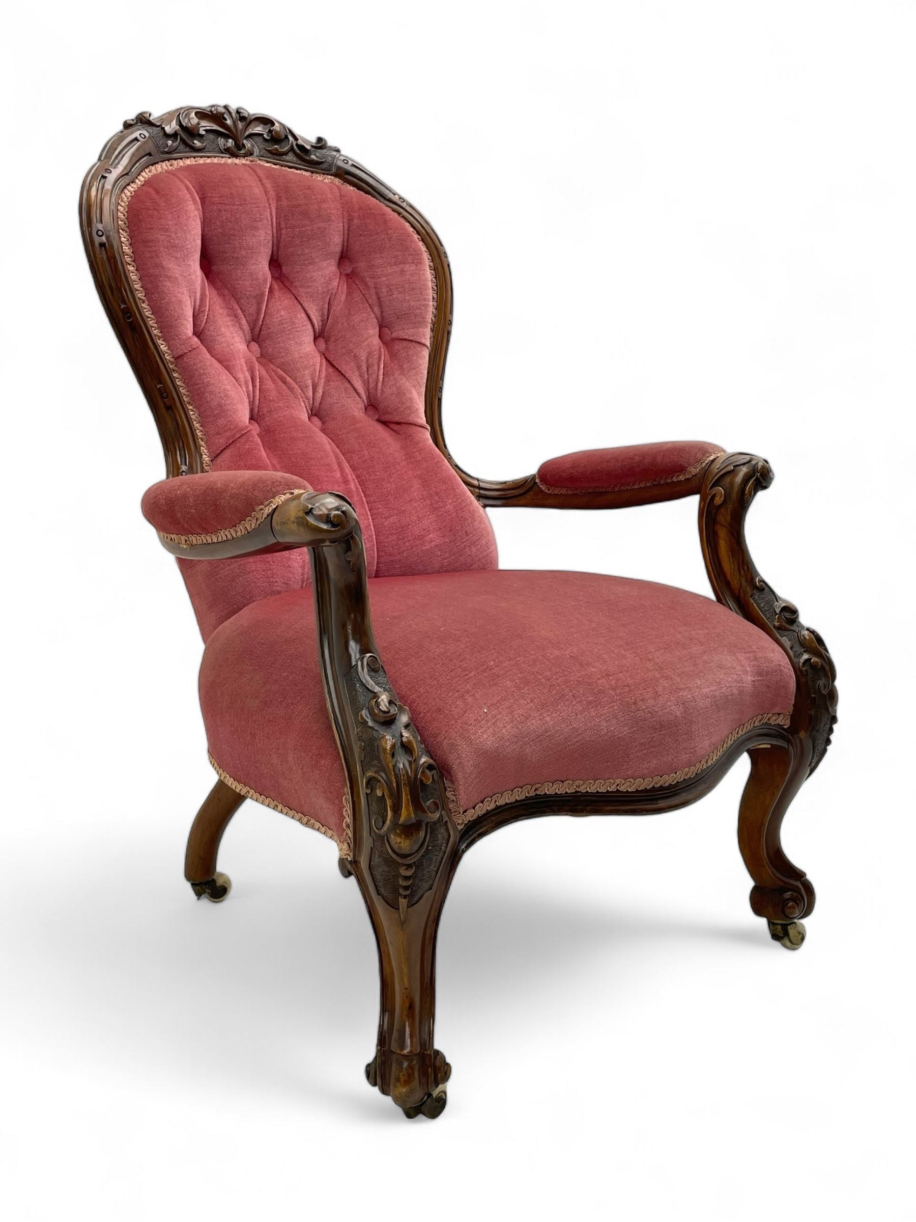 Victorian carved walnut open armchair, foliate carved cresting rail over butted back and sprung seat, upholstered in pink velvet scrolled arm terminals with moulded scrolling vines terminating to cabriole supports and ceramic castors